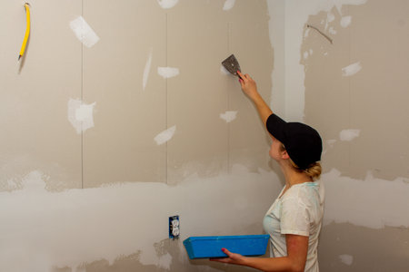 A young woman applying joint compound to a drywall as part of a kitchen remodelの写真素材