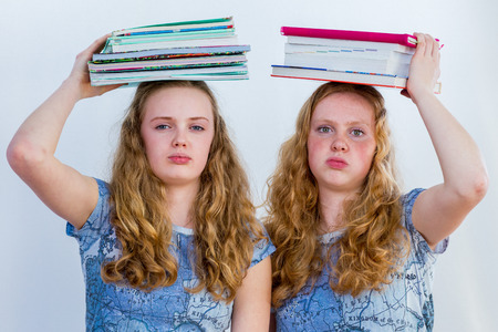 Two european sisters as schoolgirls with books on their head and a bored facial expressionの写真素材