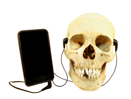 Human skull listening music on mobile device with earphones isolated on white backgroundの写真素材