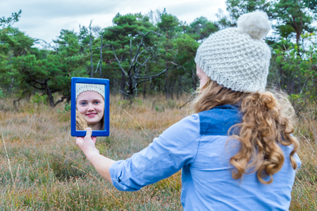 Blonde dutch teenage girl with long hair looking in mirror with forest backgroundの写真素材