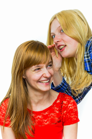 Blonde caucasian teenage girl whispering in ear of redhead girlfriend isolated on white backgroundの写真素材