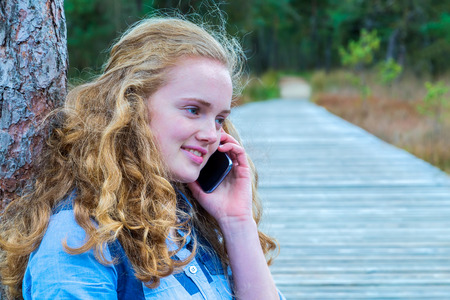 Blonde caucasian teenage girl phoning with mobile telephone in natureの写真素材
