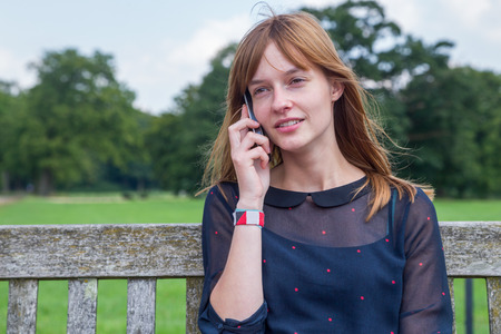 Caucasian teenage girl with red hair phoning with mobile phone in natureの写真素材