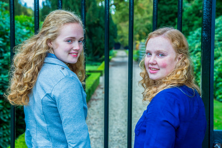 Two caucasian teenage sisterss looking back at fence of gardenの写真素材