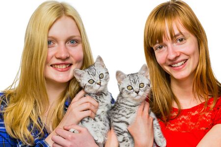 Two caucasian teenage girls showing young british shorthair black silver tabby cats isolated on white backgroundの写真素材