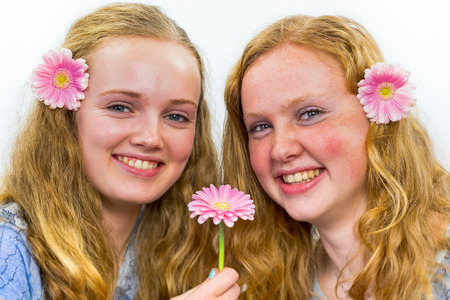 Two caucasian teenage girls laughing with pink flowers in long hair isolated on white backgroundの写真素材