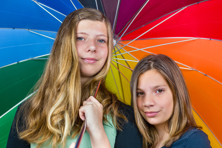 Two caucasian  teenage sisters together under colorful umbrellaの写真素材
