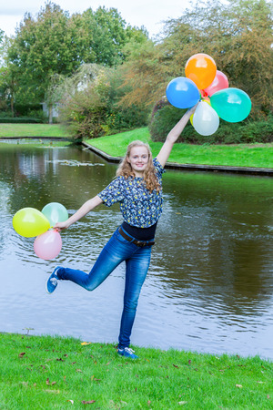 Caucasian teenage girl standing at pond in park with colored balloonsの写真素材