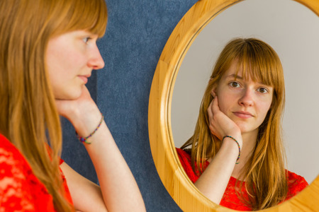 Caucasian redhead teenage girl looking in mirrorの写真素材