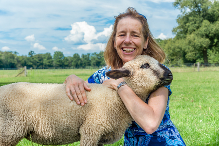 European woman embracing and hugging sheep in meadowの写真素材