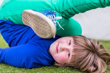 Bent european girl lying on her back on grass at playgroundの写真素材