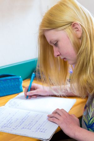Blonde caucasian schoolgirl making homework at deskの写真素材