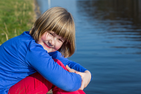 Young european girl sitting at waterfront of riverの写真素材
