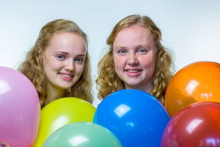 Two european teenage girls heads behind colored balloons isolated on white backgroundの写真素材