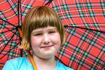 Young blonde dutch girl under red umbrella in rainの写真素材