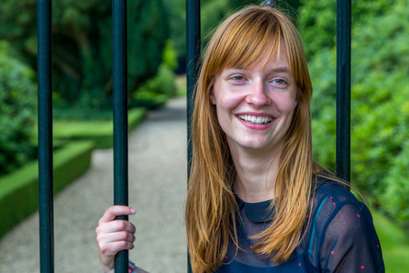 Red haired dutch teenage girl laughing holding metal bar of gateの写真素材
