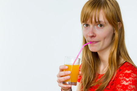 Redhead caucasian teenage girl drinking orange juice with straw isolated on white backgroundの写真素材