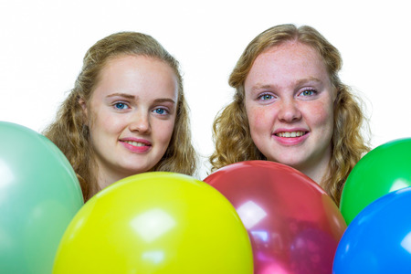 Two smiling caucasian teenage girls behind various colored balloons isolated on white backgroundの写真素材
