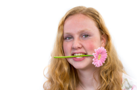 Caucasian teenage girl with pink flower in mouth isolated on grey white backgroundの写真素材