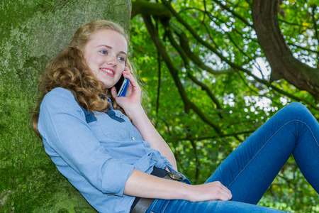 Caucasian teenage girl phoning with mobile telephone in green treeの写真素材