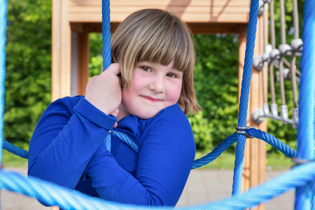 Young caucasian girl playing in web of blue ropes at playgroundの写真素材