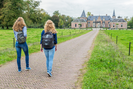 Two teenage girls walking with backpacks on road leading to castleの写真素材
