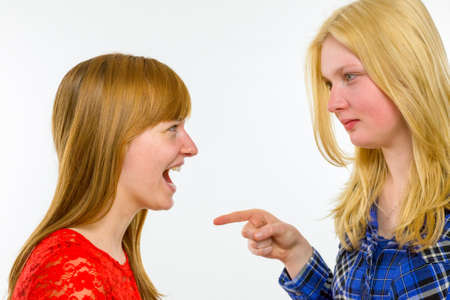 Blonde caucasian girl pointing at red haired girlfriend isolated on white backgroundの写真素材