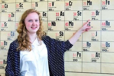Caucasian teenage girl pointing finger at periodic table in chemistry classroom at schoolの写真素材