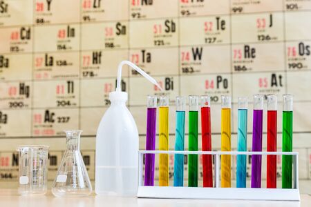Chemistry with colored test tubes and glass in front of wallchart showing periodic tableの写真素材