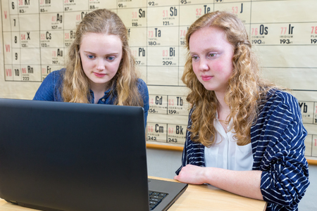 Two caucasian female students looking at computer in chemistry lessonの写真素材