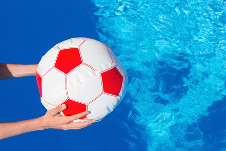 Hands of boy holding beach ball above swimming pool water invitation to playの写真素材