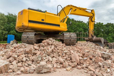 Yellow belt excavator on heap of bricks of demolished houseの写真素材