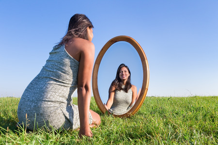 Woman kneeling on grass looking at  her mirror imageの写真素材