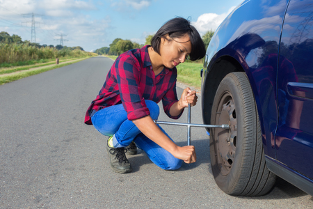 Young european woman changing car tire on country roadの写真素材