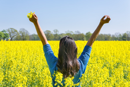 Young woman expresses happiness with arms up in yellow rapeseed fieldの写真素材