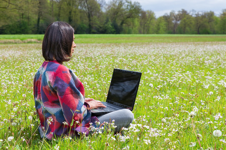 Woman sitting with laptop in pasture with white flowersの写真素材