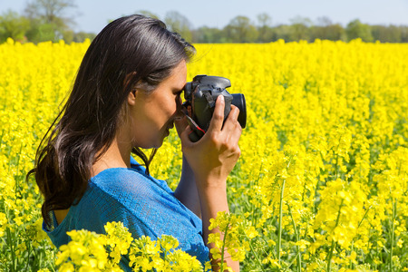 Young colombian woman with camera taking photo of yellow rapeseed field