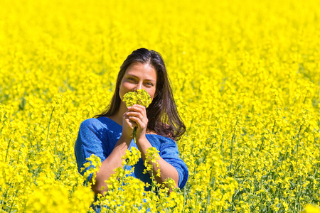 Young Colombian woman smelling yellow flowers in rapeseed fieldの写真素材