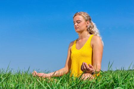 Young blond dutch woman meditating in nature with blue skyの写真素材