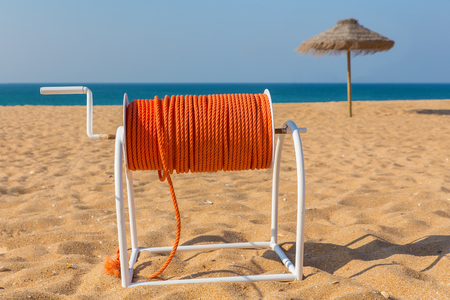 Reel with orange rescue rope on beach with parasol and seaの写真素材