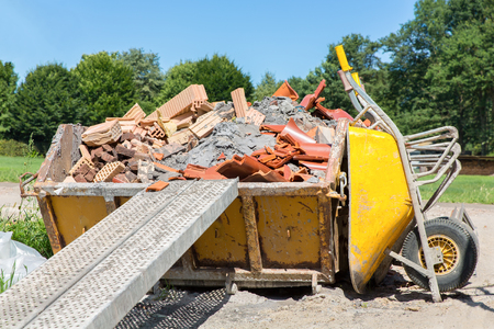 Metal container filled with rubble and wheelbarrow outsideの写真素材