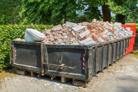 Big metal waste container filled with stones, toilet and other rubbleの写真素材