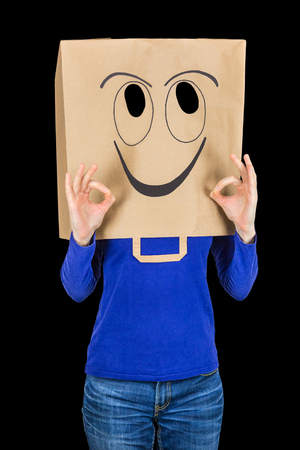 Happy woman smiling with paper bag on head isolated on black backgroundの写真素材