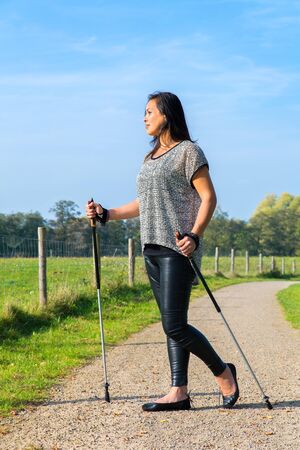 Young indian indonesian woman hiking with Nordic Walking sticks in dutch natureの写真素材
