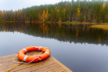 Orange life buoy lying near Finnish lake with mirror image in waterの写真素材