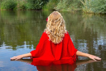 Young blonde woman in red wrap walking in natural waterの写真素材