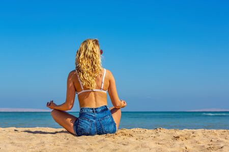 Young blonde caucasian woman with long hair meditates on egyptian beachの写真素材