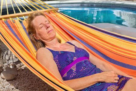 Middle aged dutch woman lying in colorful hammock near swimming poolの写真素材