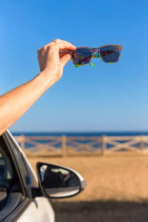 Arm in car window showing sunblinkers at shore with seaの写真素材