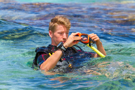 Young caucasian man as diver in sea preparing diving mask